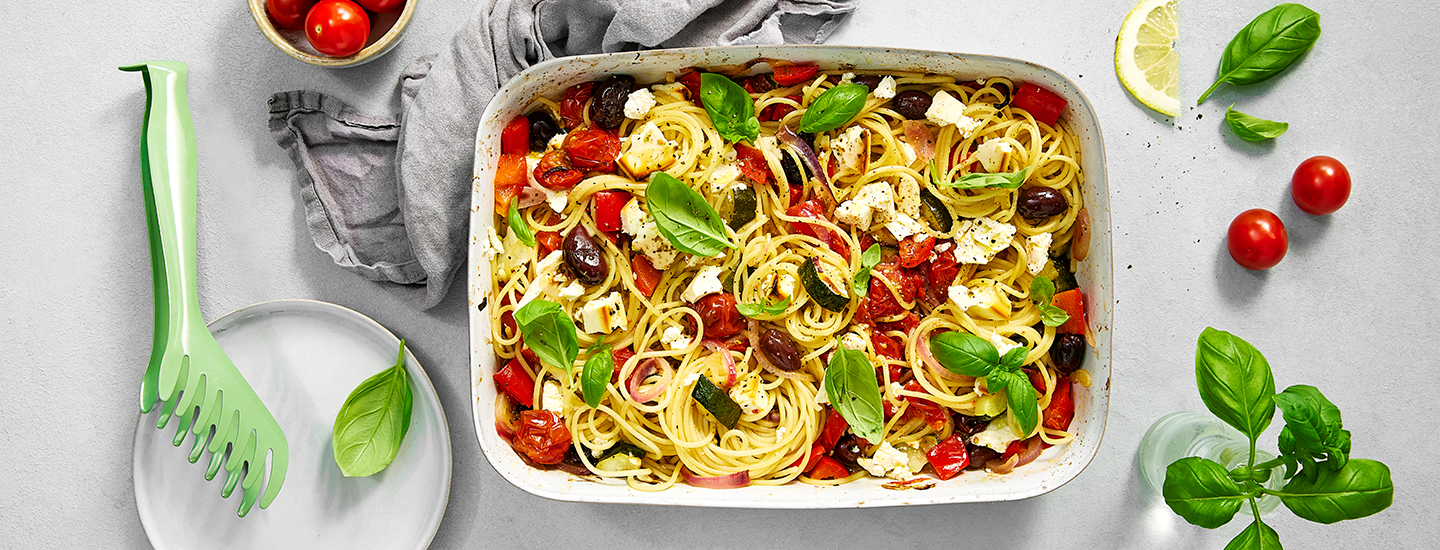 Spagettia, fetajuustoa, oliiveja ja kasviksia uunivuoassa. Pastan päälle on lisätty tuoretta basilikaa. K-Ruoka pastaresepti.
