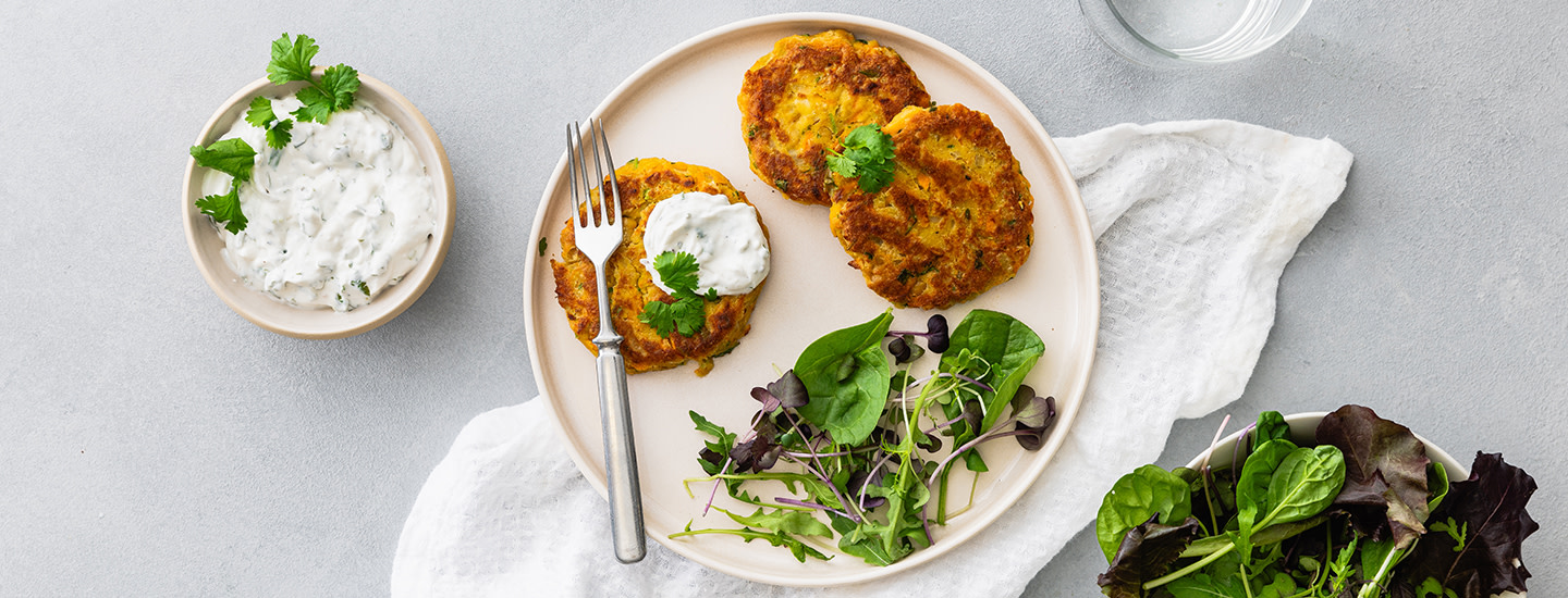 Kolme kikhernepihviä vaalealla pyöreällä lautasella. Lautasella on myös vihersalaattia. Yhden kikhernepihvin päälle on laitettu hieman kermaviilikastiketta. Lautasen vieressä on pieni syvä kulho, jossa on lisää kermaviilikastiketta. K-Ruoka arkiruokaresepti.