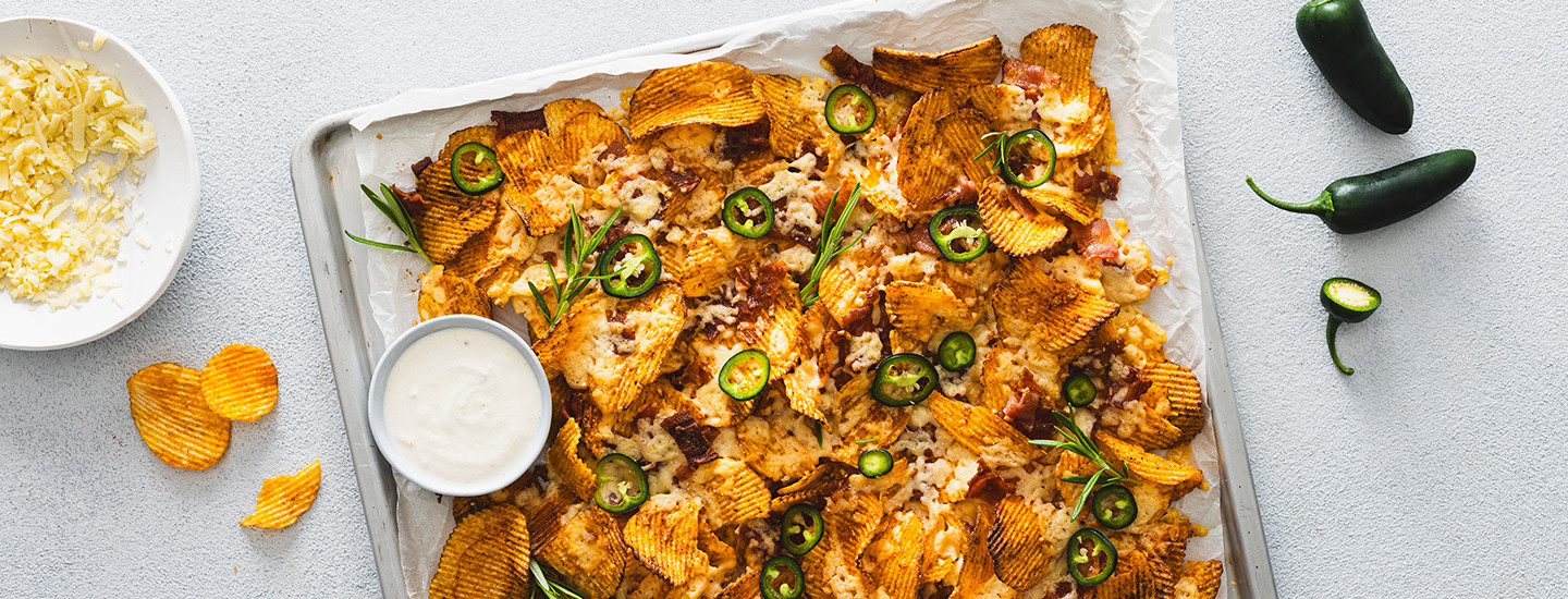 Sipsiä, pekonia, juustoa ja tuoreita jalapenosiivuja pellillä. Kaikki ainekset on paahdettu uunissa. Pellille on lisätty pieni kulho, jossa on kermaviilidippiä. K-Ruoka resepti.