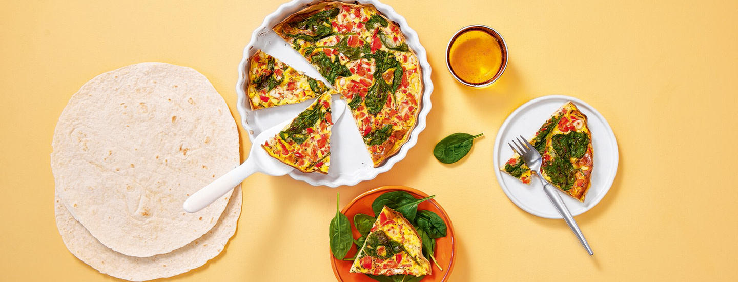 Tortillamunakas piirakkacuoassa keltaisella taustalla. Vieressä koristeela tortillalettuja sekä piirakkapalat. K-Ruoka kananmunaresepti.