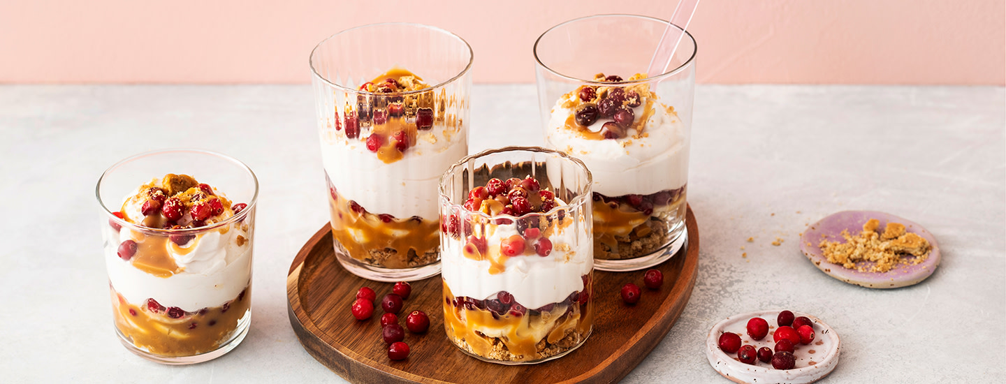 Karpalo-kinuskibanoffeeta kolmessa tarjoilulasissa. Karpalot, keksimuru, banaaniviipaleet, kinuski ja kinuskirahka on ladottu lasiin päällekkäin. K-Ruoka jälkiruokaresepti.