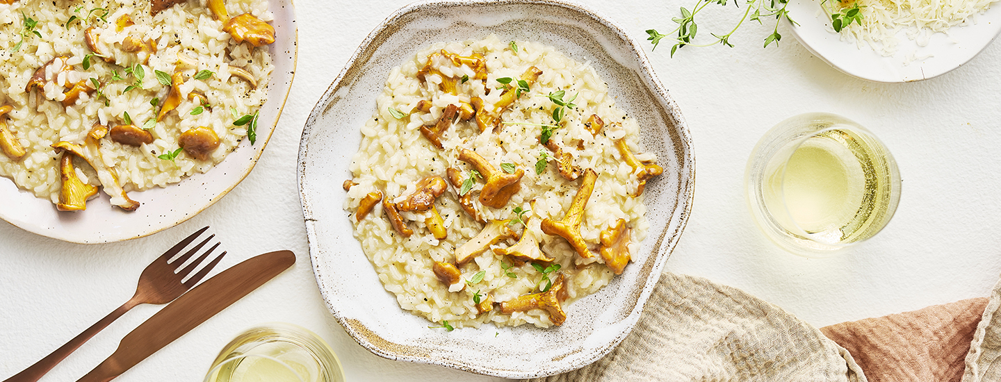 Kantarellirisottoa vaalealla lautasella. Risoton päälle on aseteltu kokonaisia pieniä kantarelleja ja parmesaaniraastetta. K-Ruoka risottoresepti.