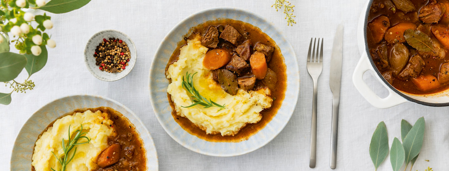 Pippurista karjalanpaistia ja perunamuusia vaaleansinisellä lautasella. Lautasen oikealla puolella on haarukka ja veitsi, vasemmalla puolella pieni kulho, jossa on kokonaisia pippureita. K-Ruoka arkiruokaresepti.