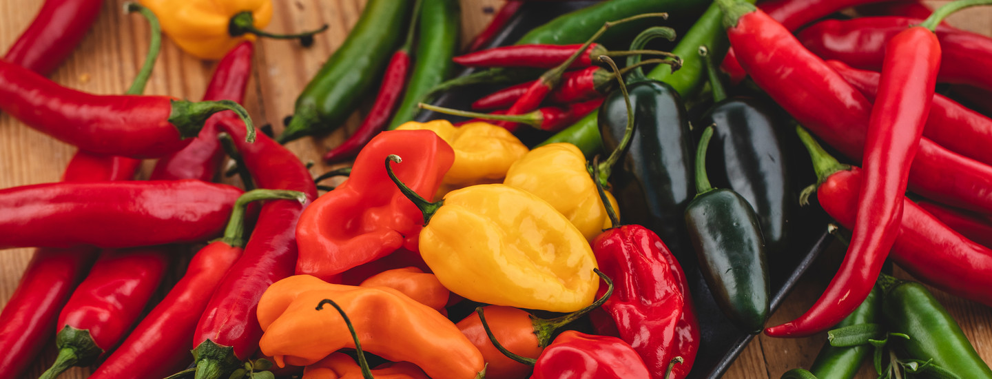 Erilaisia tuoreita chilejä yhdessä puisen pöydän päällä. K-Ruoka raaka-aine.