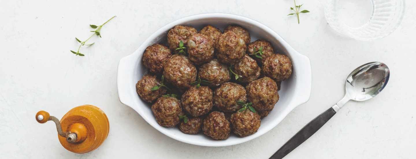 Lihapullat valkoisella lautasella vaalealla taustalla. Ympärillä somisteena aterimet, lasi ja maustemylly. K-Ruoan reseptikuva.