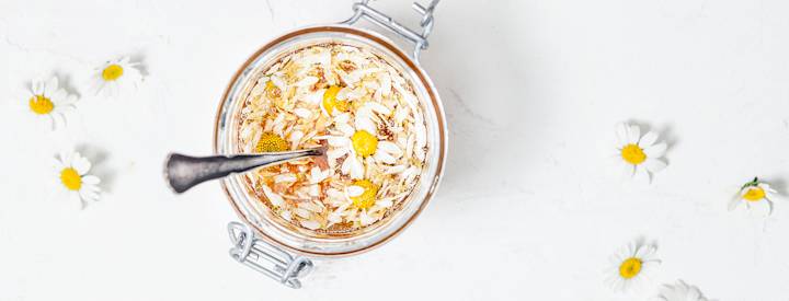 Syötäviä kamomillan kukintoja lasipurkissa. Kukintoja on keitetty ja mukaan on lisätty hunajaa.