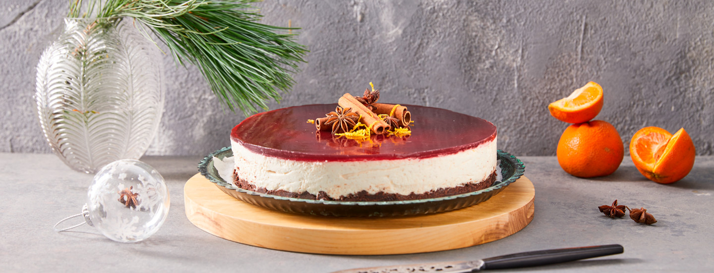 Vegaaninen glögijuustokakku kakkulautasella, joka on puisen tarjoiluastian päällä. Juustokakussa on tummanruskea keksipohja, vaalea täyte ja tummanpunainen glögikiille. K-Ruoka jouluinen juustokakkuresepti.