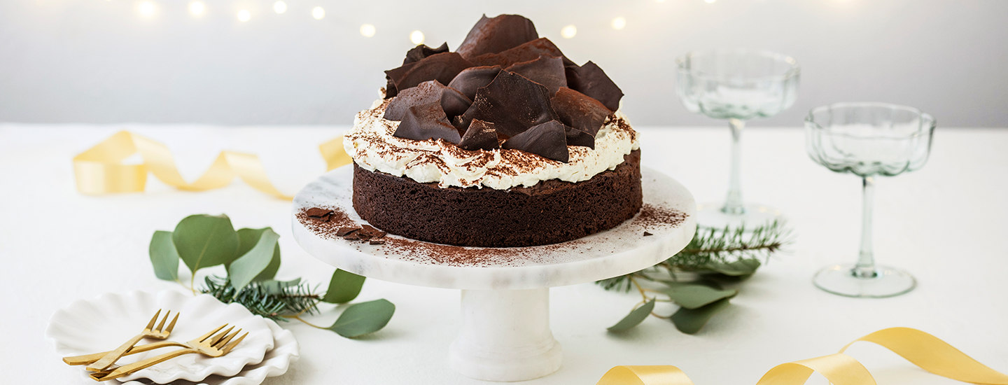 Kakkutarjottimella on suklaakakku, jonka päälle on laitettu kermavaahtoa ja suklaakoristeita. Kermavaahdon päälle on ripoteltu kaakaojauhetta. K-Ruoka jouluresepti.