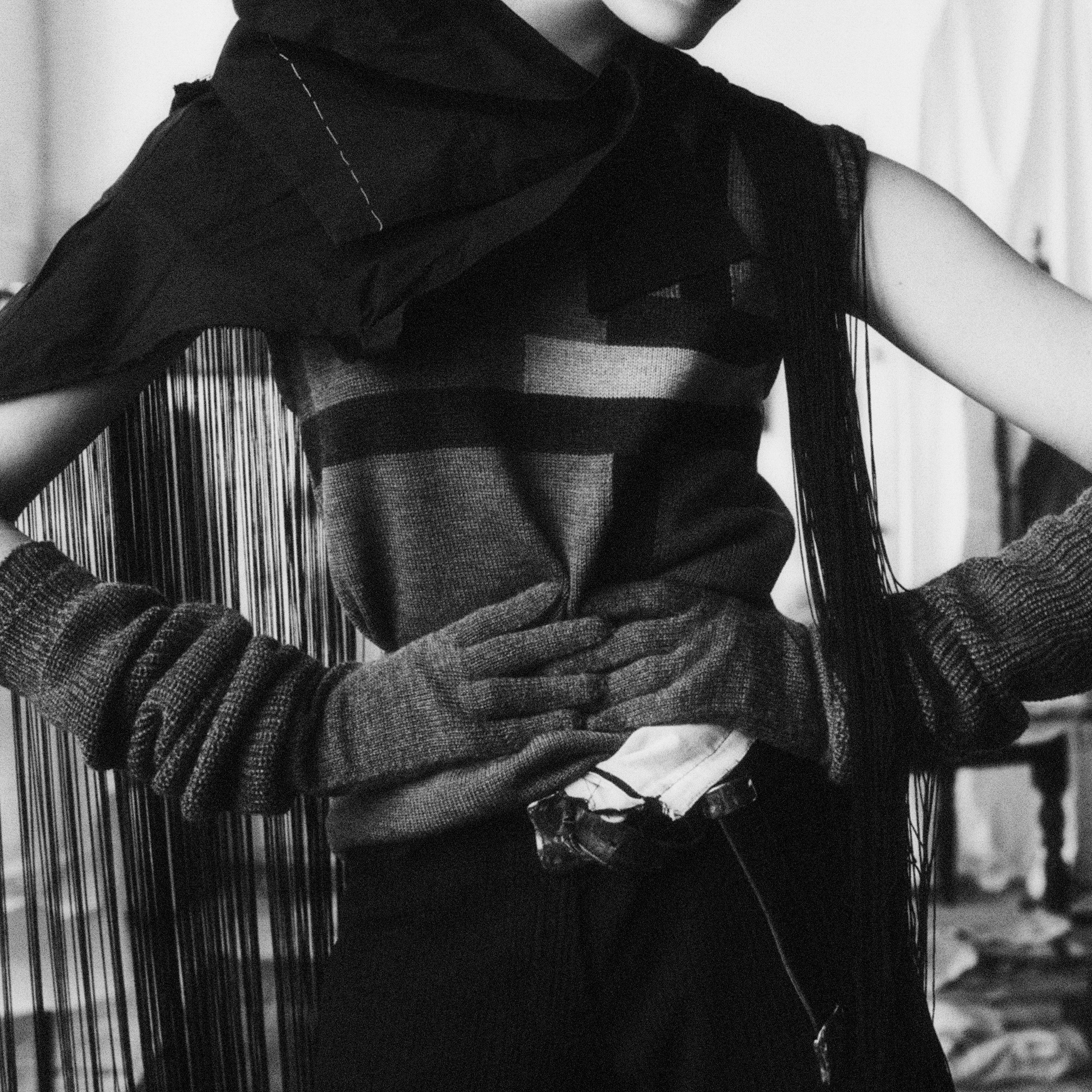 The image is a close up of the model's torso, she is holding her waist and wearing thick gloves. There are a lot of textures and knits. 