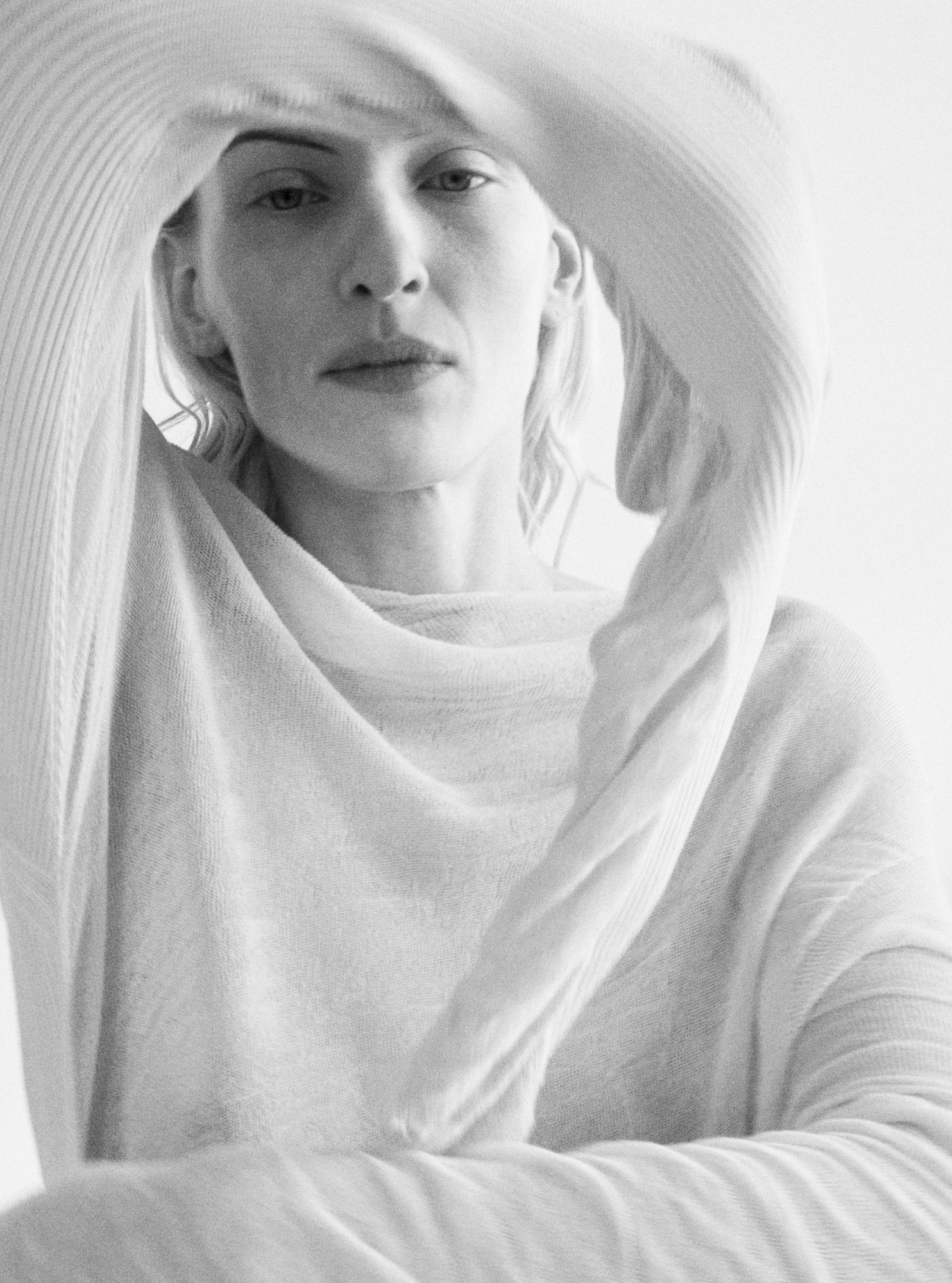 Model is wearing a light colored sweater. Model is facing the camera and has her arm up covering her forehead. She is pulling on the bottom section of her sleeve. 