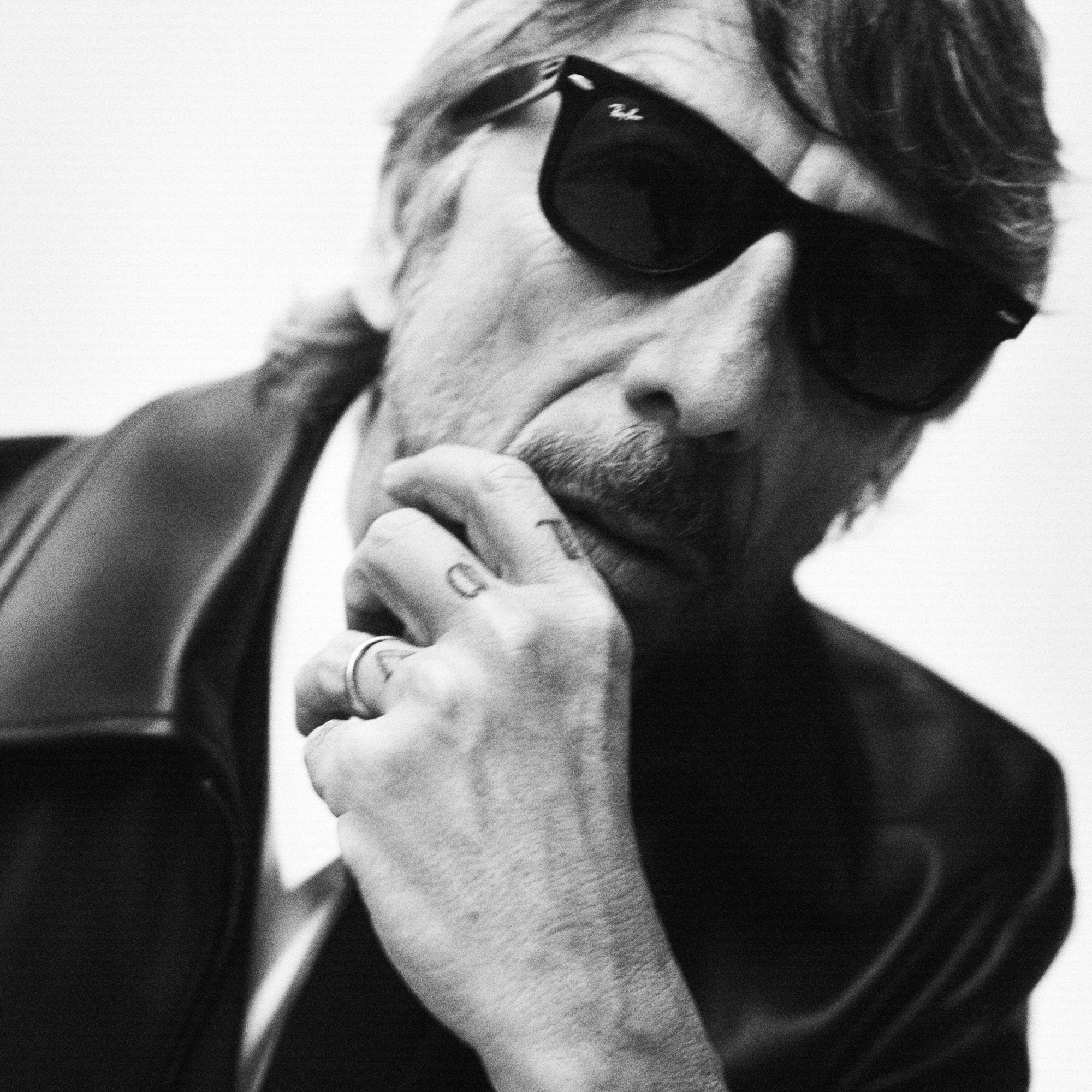 Portrait of Pierpaolo Piccioli wearing sunglasses and leaning towards the camera. His hand is resting on his chin. 