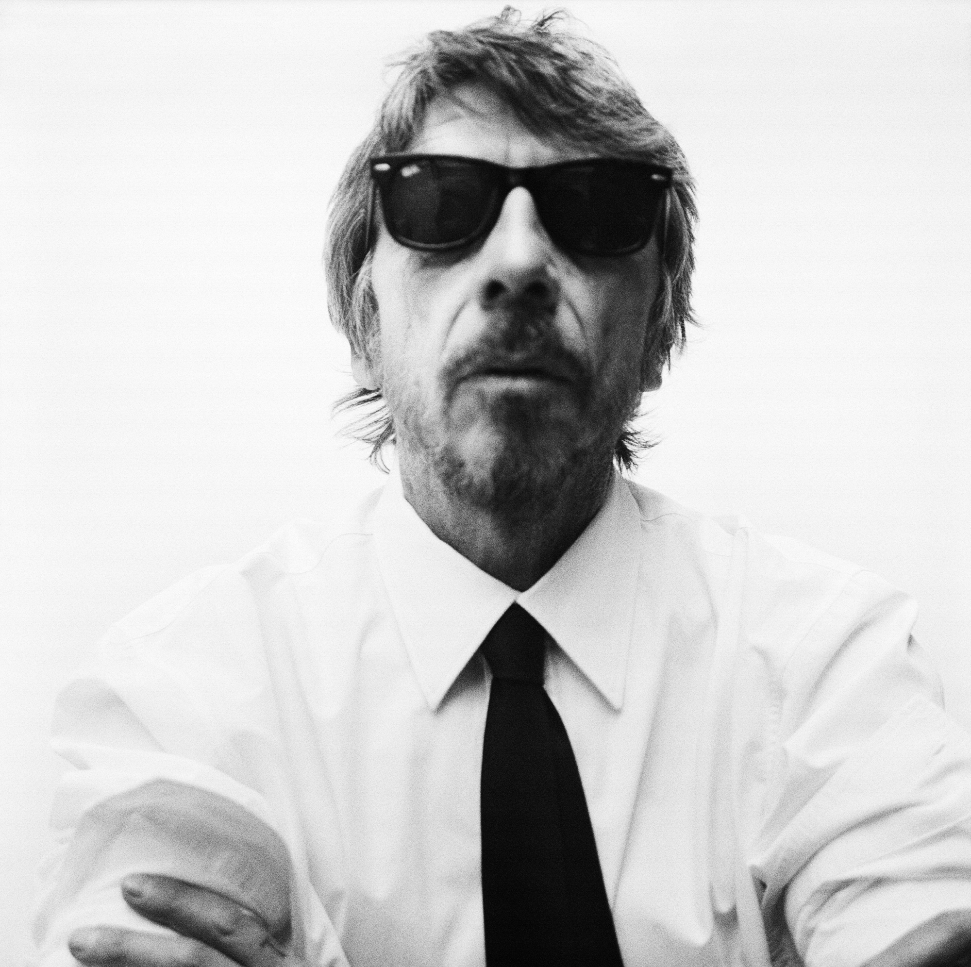 Portrait of Pierpaolo Piccioli wearing a white shirt with a black tie. He is looking directly towards the camera wearing sunglasses. 