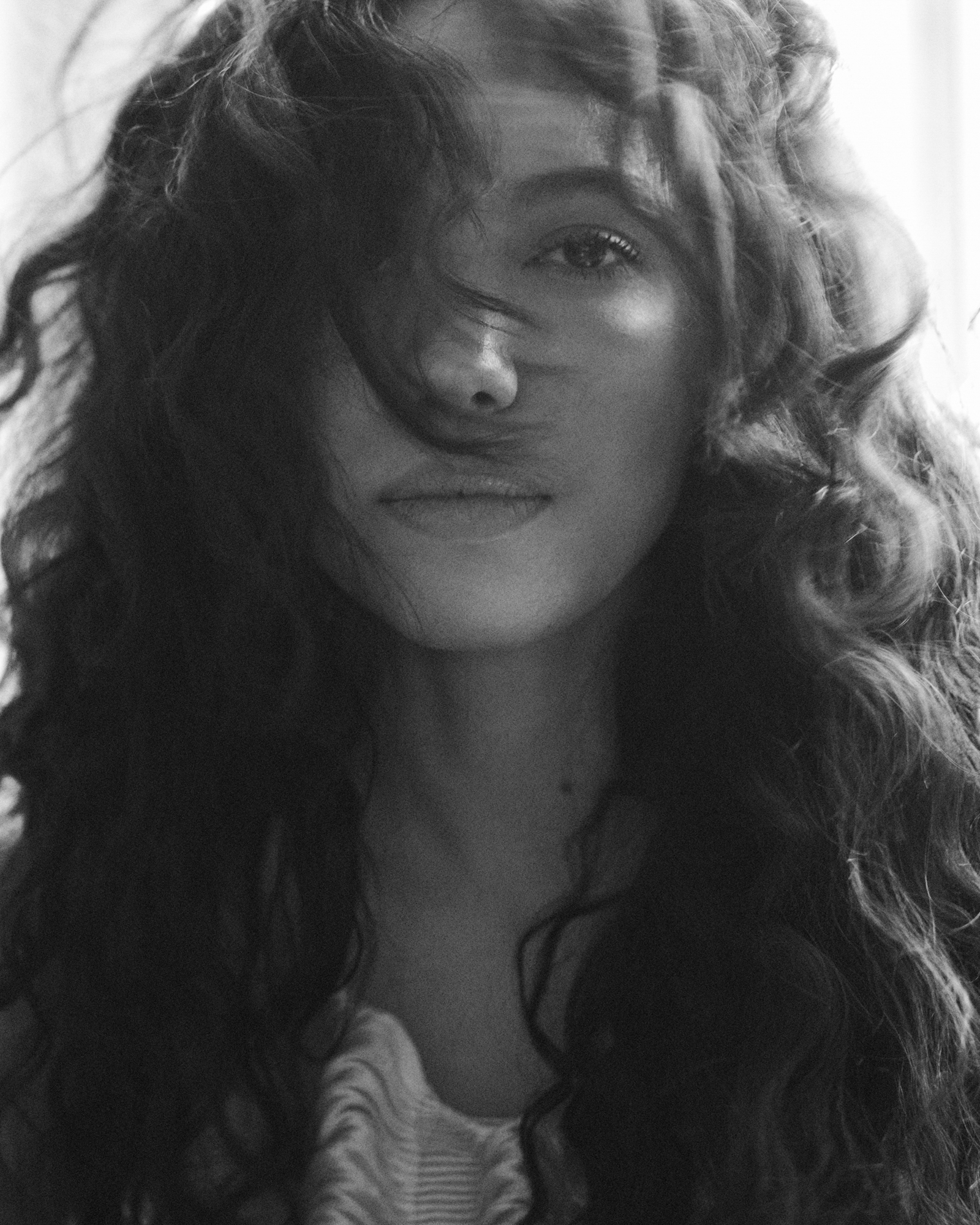 The image is a close up portrait of Jurnee Smollett. She is looking straight at the camera, and hair is blowing in her face slightly, partially obscuring her face. 