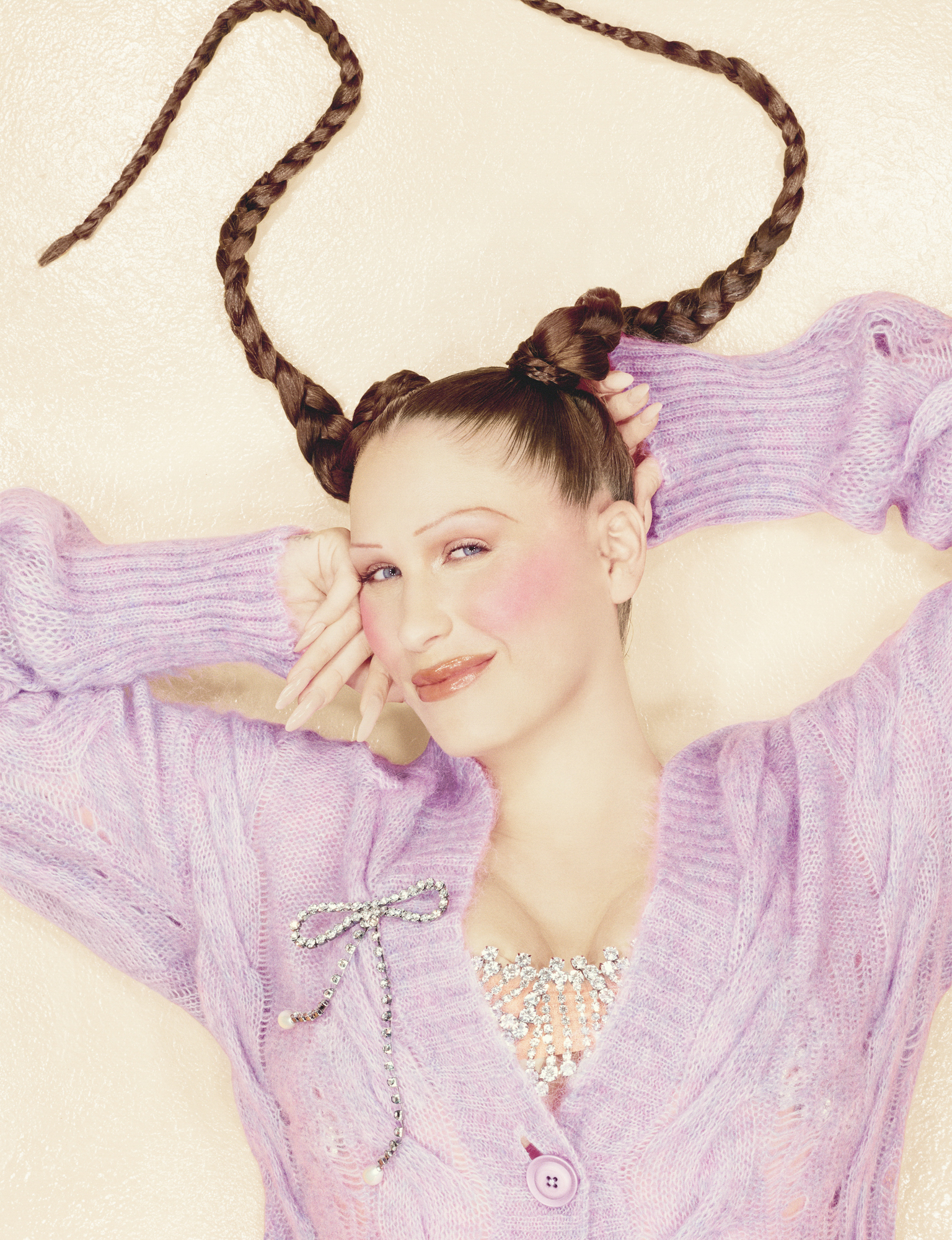 Eartheater is laying on the ground with a purple button up cardigan. She has her hands on either side of her head. She is looking up with a smile at the camera. 