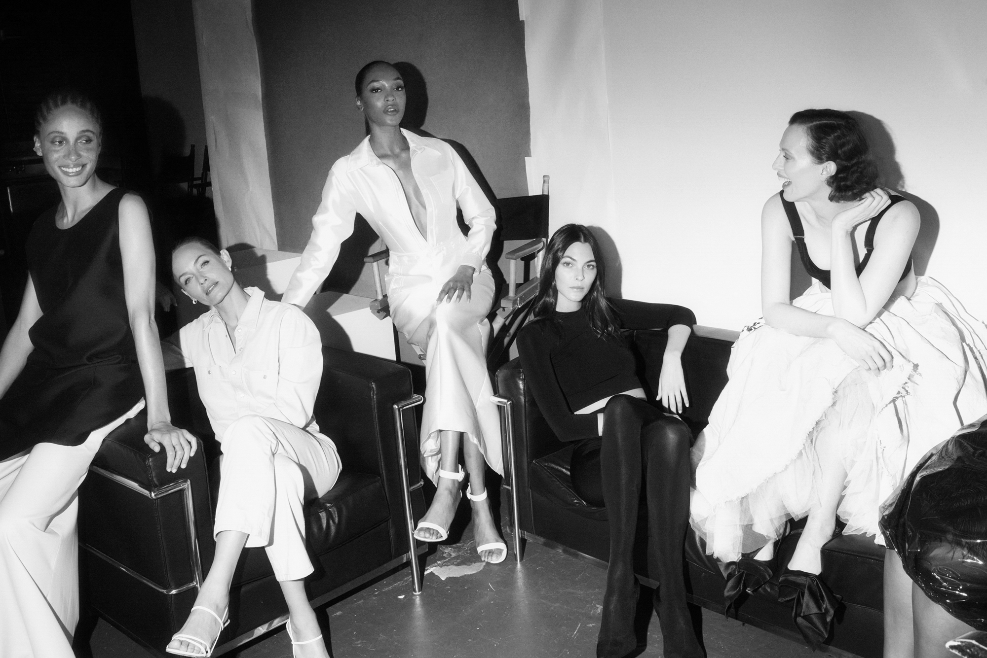 Adwoa Aboah, Amber Valletta, Jourdan Dunn, Vittoria Ceretti, and Karen Elson are seated in a lounge area. The women are sitting on black leather couches with metal fixtures. 

