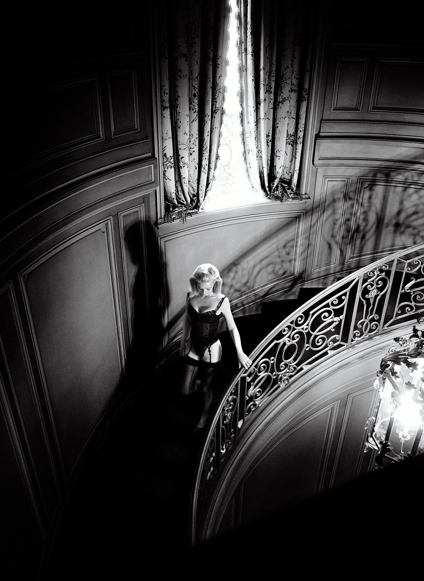 Gwyneth Paltrow is descending a curved staircase. She is seen from above, and light is coming from a window above with heavy curtains. 