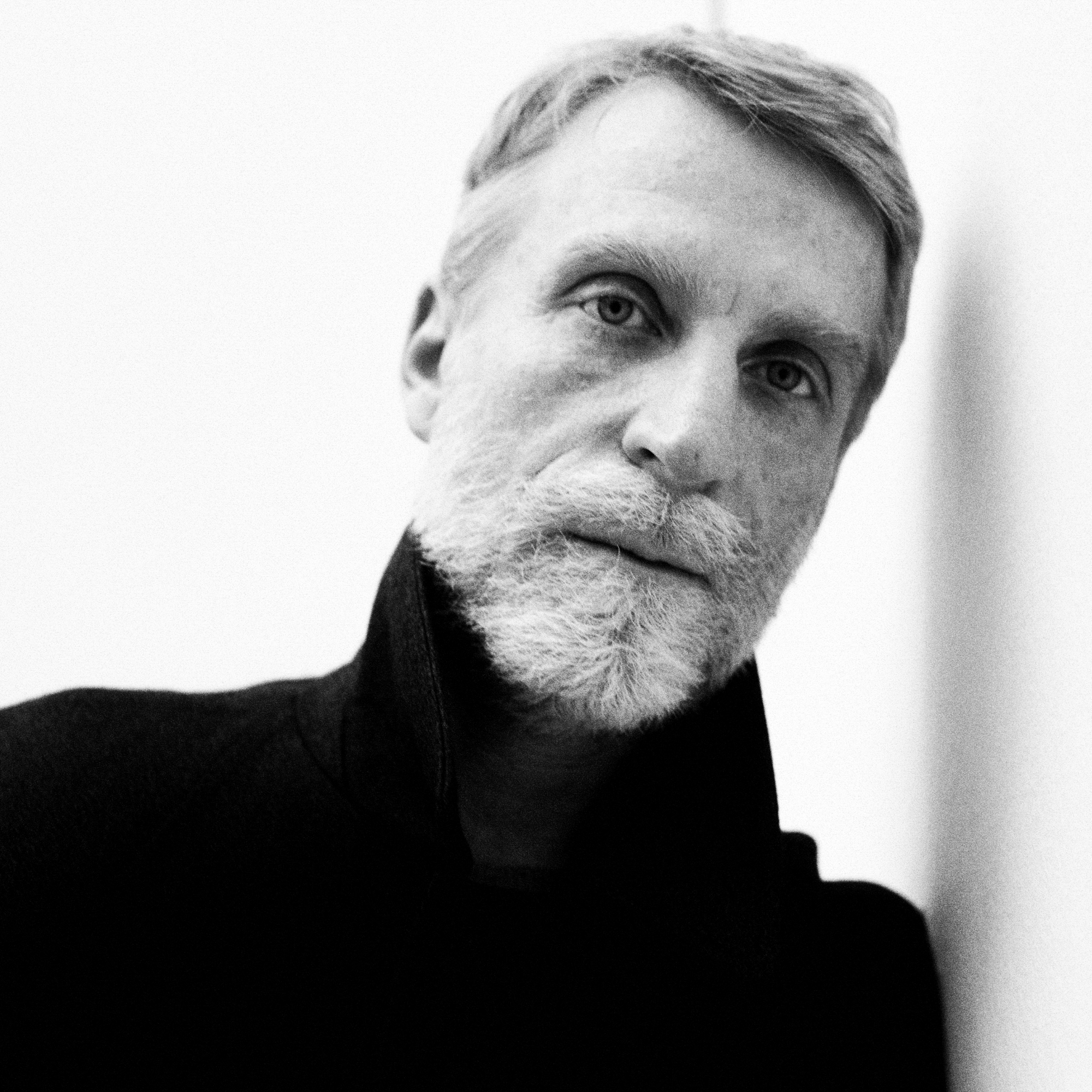 Portrait of Simone Bellotti leaning against a white wall looking directly at the camera. 