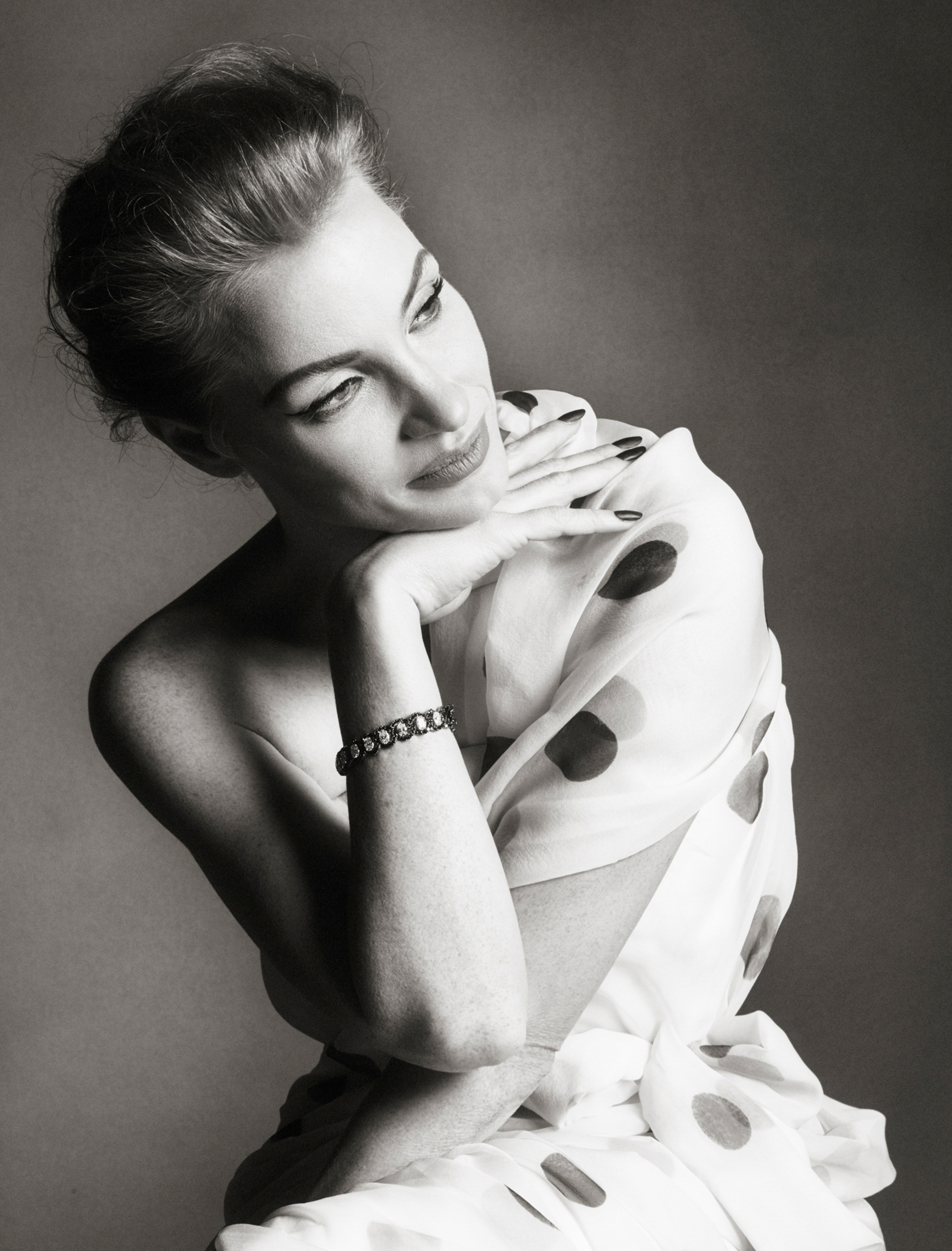 Jessica Chastain is leaning forward slightly and resting her chin on the back of her hand. She is wearing a white polka dot dress and looking in the distance on the right side of the frame. 