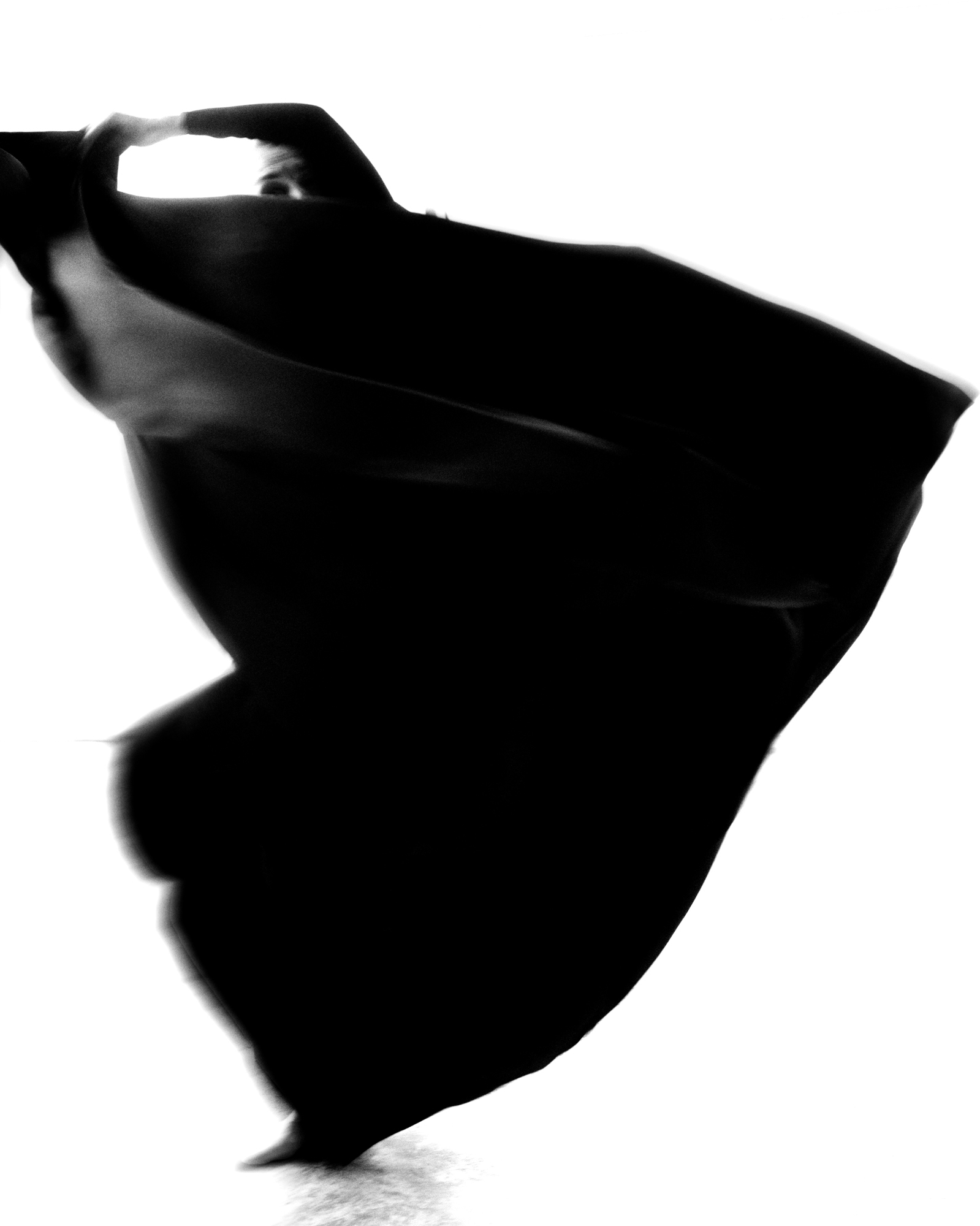 Figure in a large black garment is moving across the frame. Motion blur is obscuring the figure's body. 
