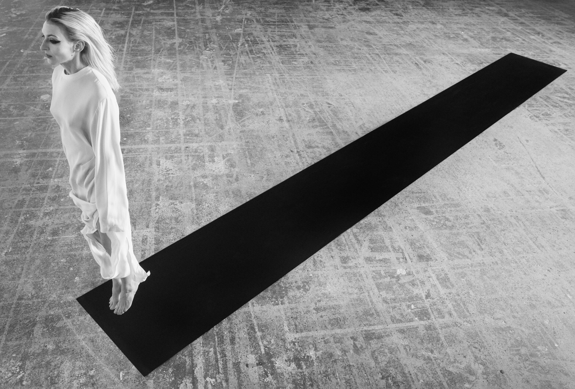 A woman dressed in all white is standing on her toes at the end of a black rectangular carpet. The woman is on the left hand side of the frame. 