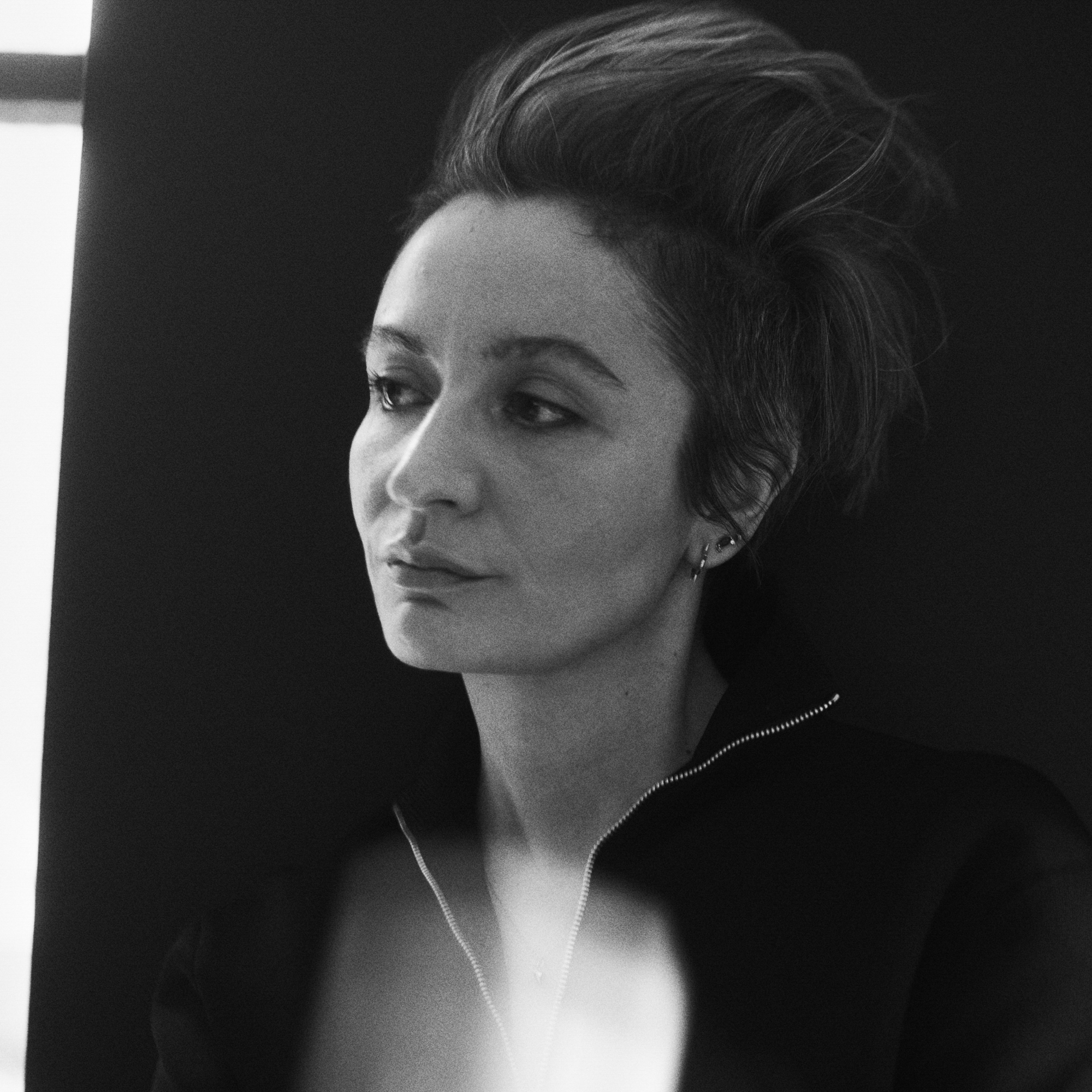 Portrait of Veronica Leoni in front of a black backdrop looking away from the camera. 