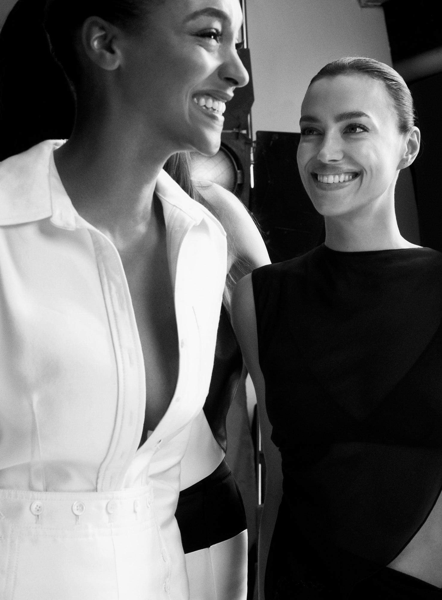 Irina Shayk is smiling up at Jourdan Dunn. Both women take up the majority of the left and right side of the image. The studio and equipment is slightly visible in the background. 