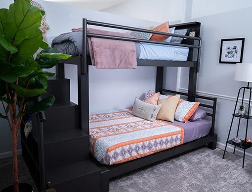 A charcoal Twin XL Over Queen Adult Bunk Bed with stairs in a guest bedroom seen from the lower left-hand corner.