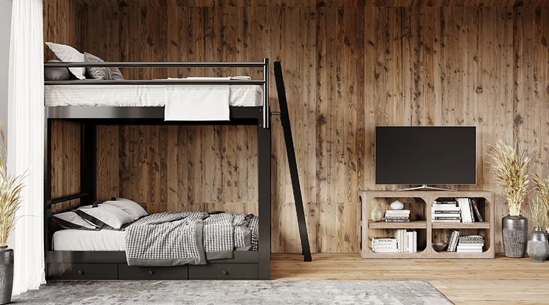 A black Queen Over Queen Adult Bunk Bed with three drawers beneath the bed frame in a mountain home with wood-paneled walls seen from the right side of the bed frame from a distance.