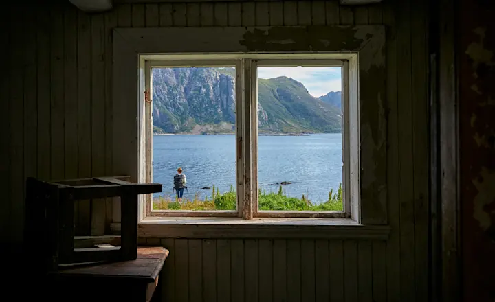 Shot of a window inside an older cabin looking out at a beautiful lake.
