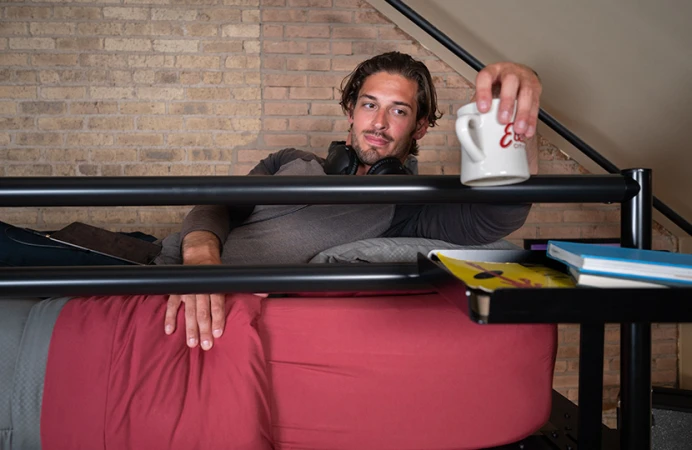 A man on his black queen Adult Loft Bed putting a coffee mug down on his tray accessory