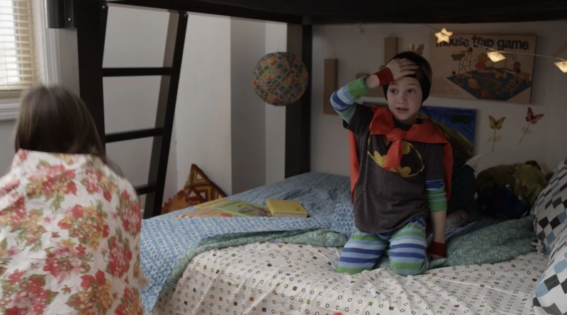 A young boy dressed as a superhero sits on the bottom bunk of a black Adult Bunk Bed preparing to chase his older sister who is wrapped in a comforter