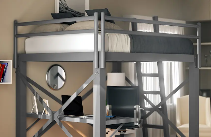 A modern loft bed with a metal frame in a cozy room. Below the bed is a compact workspace with a desk and chair. The room also features bookshelves, decor items, and a window allowing natural light in.