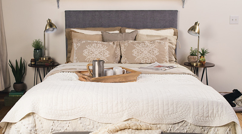 A white Platform Bed with a gray fabric headboard in a nice urban bedroom with a tray for coffee and newspaper lying on the bed seen close up directly from the foot of the bed.