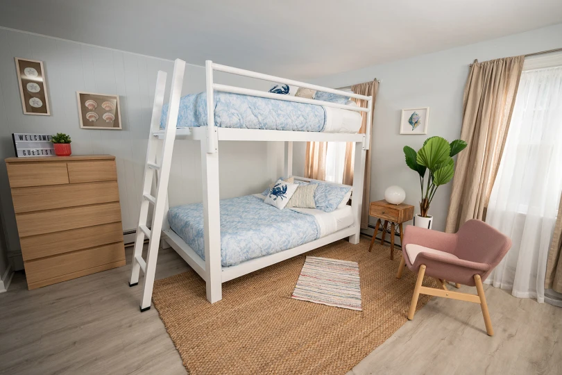 A white Adult Bunk Bed in a beach house bedroom. Seen from the right-hand side from a slight angle toward the lower corner.