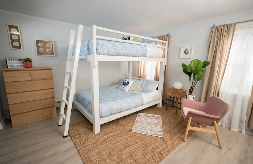 A white Adult Bunk Bed in a beach house bedroom. Seen from the right-hand side from a slight angle toward the lower corner.