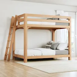 A light colored queen over queen size Wood Bunk Bed for Adults in a nice, open, airy room with a lot of natural light and no other furniture. Seen from the left-hand side of the bed at a slight angle toward the foot of the bed frame.