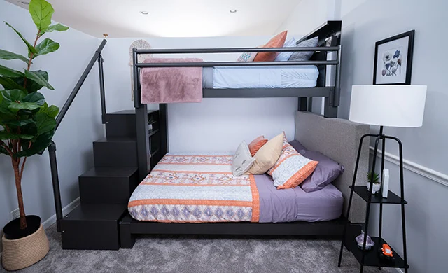 A charcoal Twin XL Over Queen Adult Bunk Bed with stairs in a guest bedroom seen directly from the side.