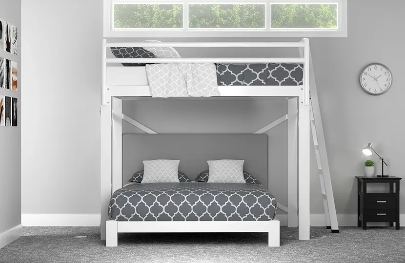 A white Full Over Queen L-Shaped Bunk Bed with light gray bedding in a basement guest room with gray walls. Seen head-on from the foot of the bottom bunk.