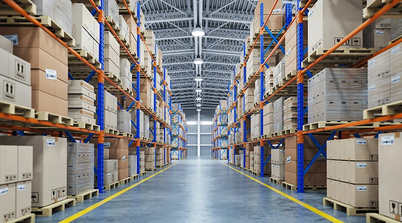 A straight shot down a huge warehouse aisle with rows of shelves full of large boxes on each side.