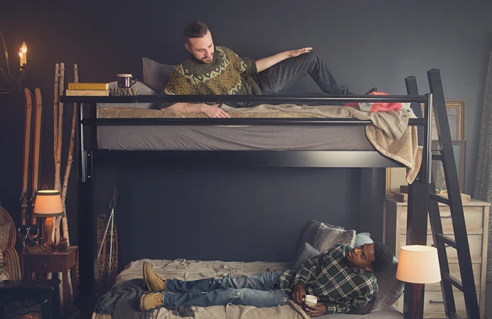 Two Young adult men on a black Queen Over Queen Bunk Bed for adults in a ski lodge bedroom, each lying on a bunk and looking at each other talking.