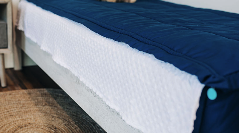A close up shot of blue zipper bedding with the white comfort panel section pulled out and draped over the side of the bed frame.