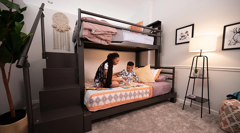 A mother and her young son reading a book on the bottom bunk of a Charcoal Twin XL Over Queen Adult Loft Bed in a guest bedroom.