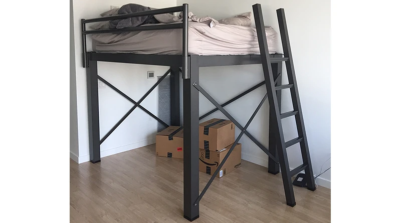 A charcoal queen size Adult Loft Bed stands in a mostly empty room with three unopened moving boxes on the floor in the space beneath the bed.