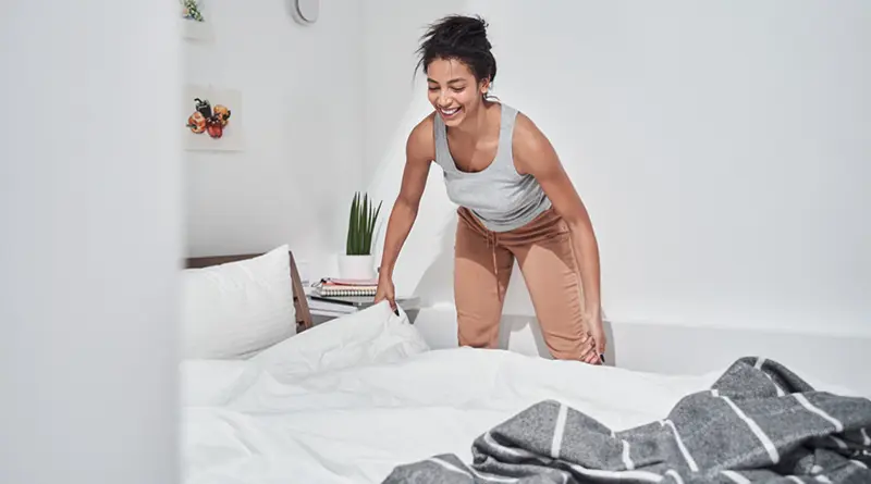 A young woman applying a white comforter to her bed and dressing it nicely.