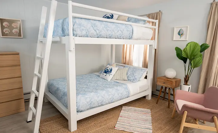 White Adult Bunk Bed in a beach house guest room dressed in light blue and white coastal bedding seen from the lower left-hand corner of the bed at a slight distance.