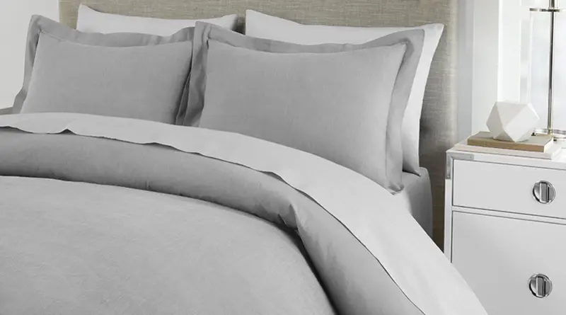 A light gray duvet and pillow sham set laid out on a queen size bed over white sheets and white pillow cases.