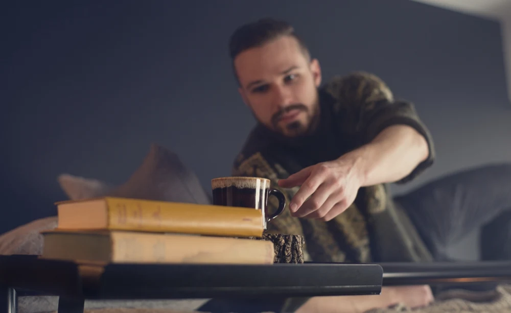 A man on the top bunk of an Adult Bunk Bed reaching for his cup of coffee sitting on an attached matching tray accessory.