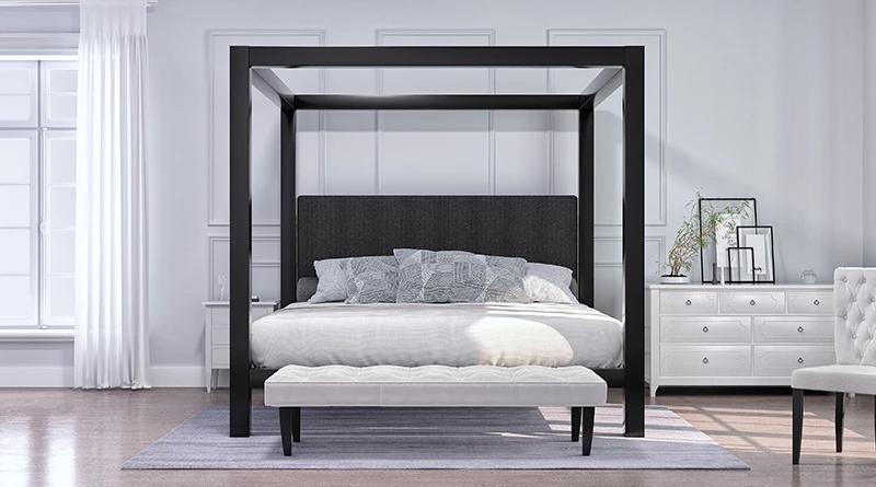 A black Wyoming King size metal four poster Canopy Bed in an upscale master bedroom space with a minimalist black-and-white aesthetic surrounded by mostly white walls, dressing, and furniture. Seen directly from the foot of the bed.