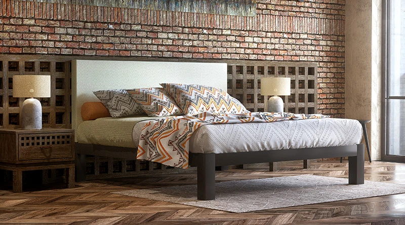 A charcoal Wyoming King Bed with a beige headboard seen from the front right corner in a rustic hotel room with a brick wall background.