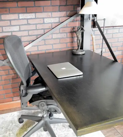 An Adult Loft Bed with desk under the bed. Close up image of the desk, which has an office chair next to it and a lamp and laptop on top of the desk. 